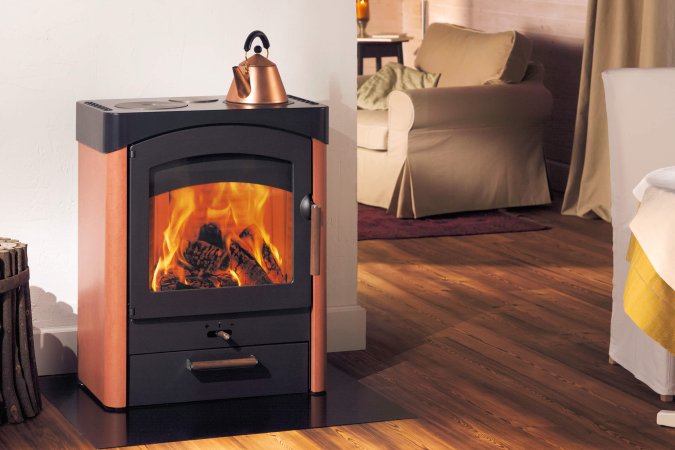 Pallas stove ambiance photo with ceramic cladding, with wood drawer and kettle on hotplate